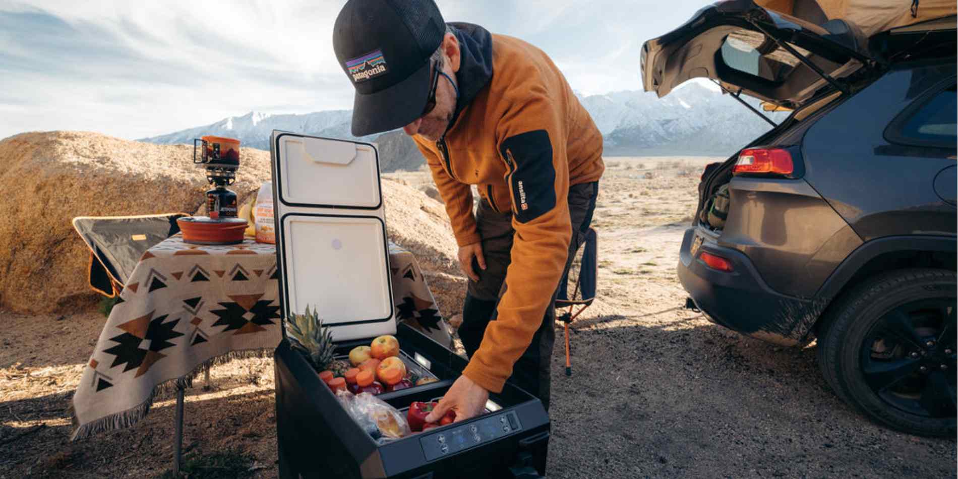 A man takes fruits out of a BougeRV 12V electric car cooler while camping with his car